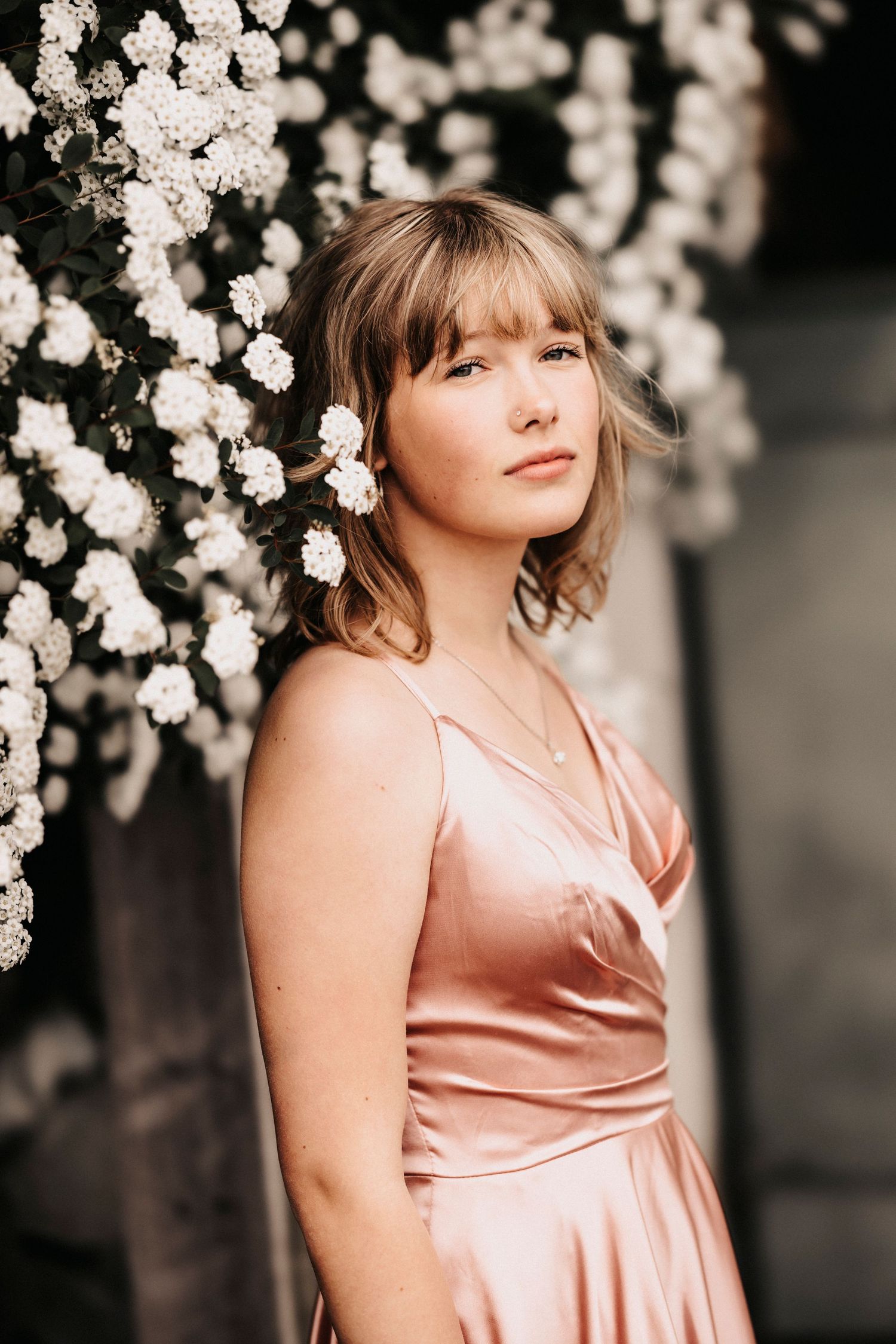 Portrait against blooming white flowers wearing pink satin dress.