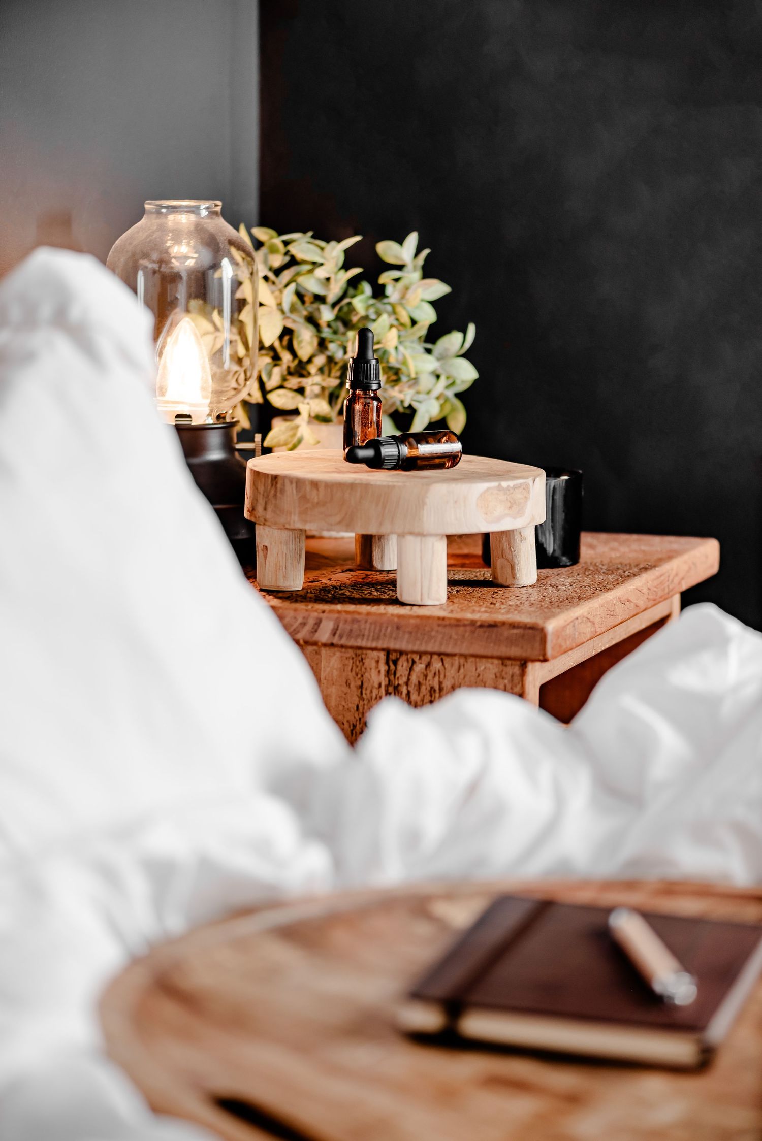 Close up of essential oils on bedside table with journal out of focus and plants. Serene, soothing, zen, mindful