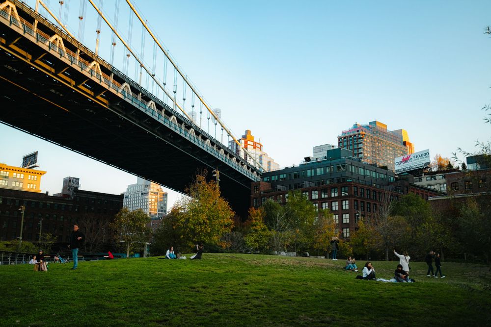 Wide panoramic view of Brooklyn Bridge Park with bridge spans and Manhattan skyline in background.