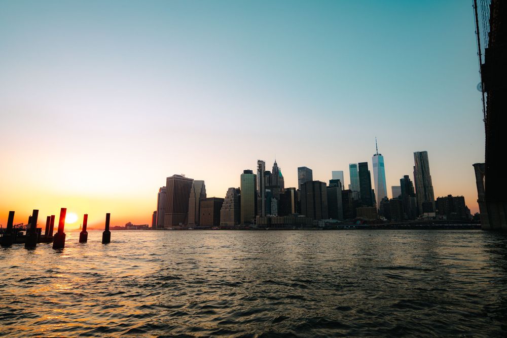 Panoramic cityscape silhouette reflected in water during golden hour.