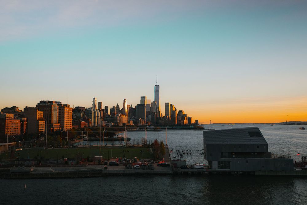 Urban skyline stretches across the horizon at dusk with water in the foreground.