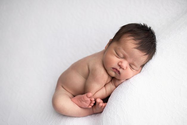 Newborn baby girl on a white blanket curled up showing her little toes.
