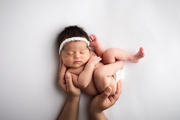 Newborn baby girl curled up in mom's hands.