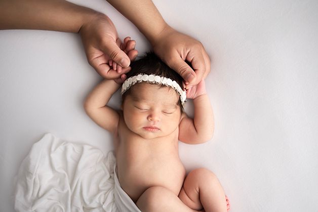 Newborn baby girl laying on her back on a white blanket holding mom's fingers.