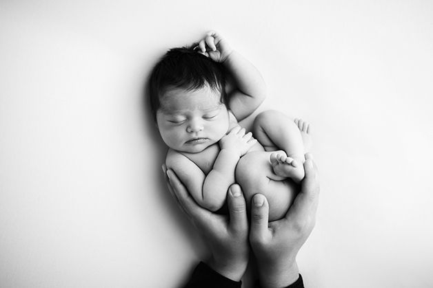 Black and white image of newborn baby girl curled up in her dad's hands.