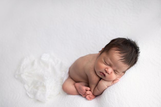 Newborn baby girl posed on her belly with her tiny toes showing and her cute little face.