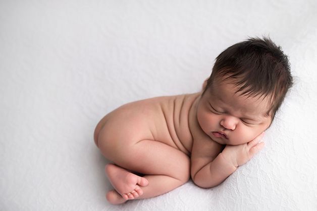 Newborn baby girl on her belly with her little hand rested under her cheek.