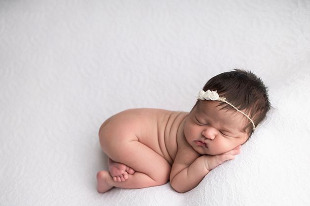 Newborn baby girl curled up showing her back rolls on a white blanket.