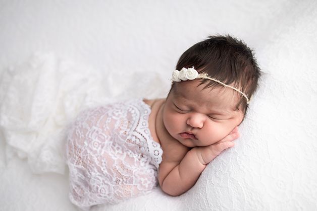 Newborn baby girl on a white blanket with a lace wrap draped over her back.