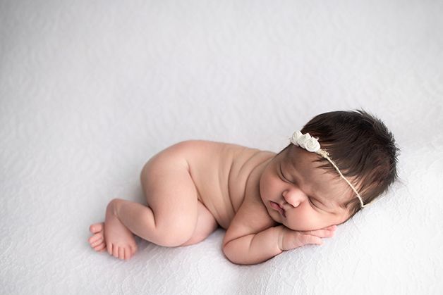 Newborn baby girl sleeping on her side on a white blanket.