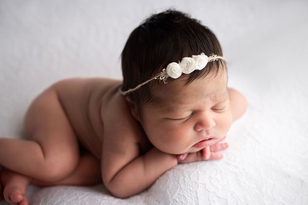 Newborn baby girl with her head resting on her hands.  Light is coming in from the side.