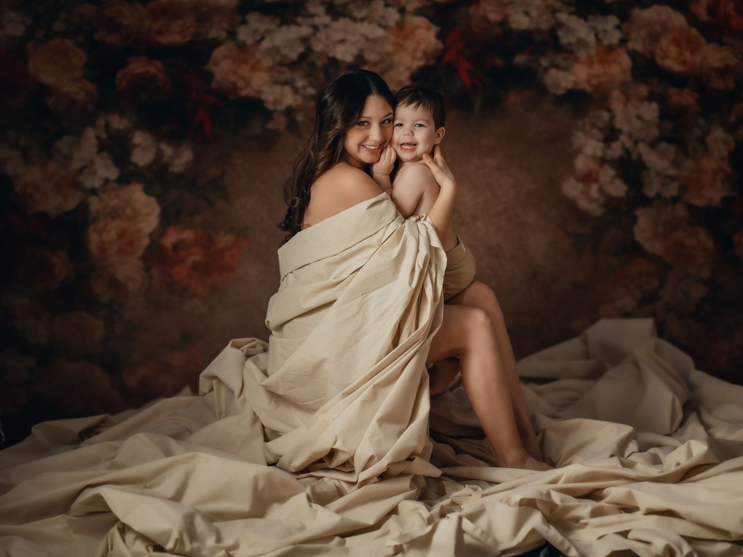 Mother joyfully holding her baby, wrapped in soft fabric, in a classic fine art portrait. Toronto motherhood photography.