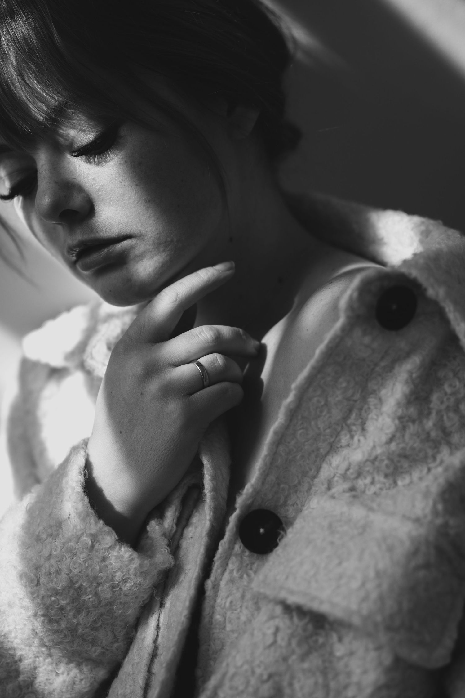 Dramatic black and white close-up portrait of someone in textured white jacket with contemplative expression.