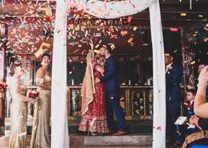 Joyful wedding celebration under white arch with red confetti shower during ceremony exit.