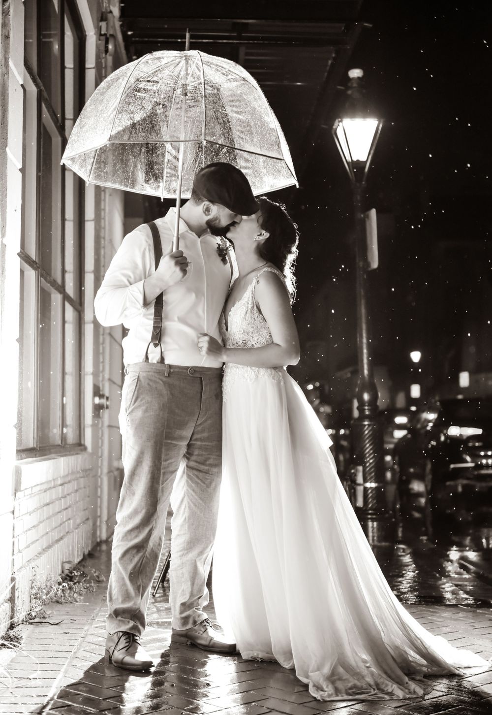 Couple sharing an intimate moment under a clear umbrella on a rainy evening with street lamps glowing.