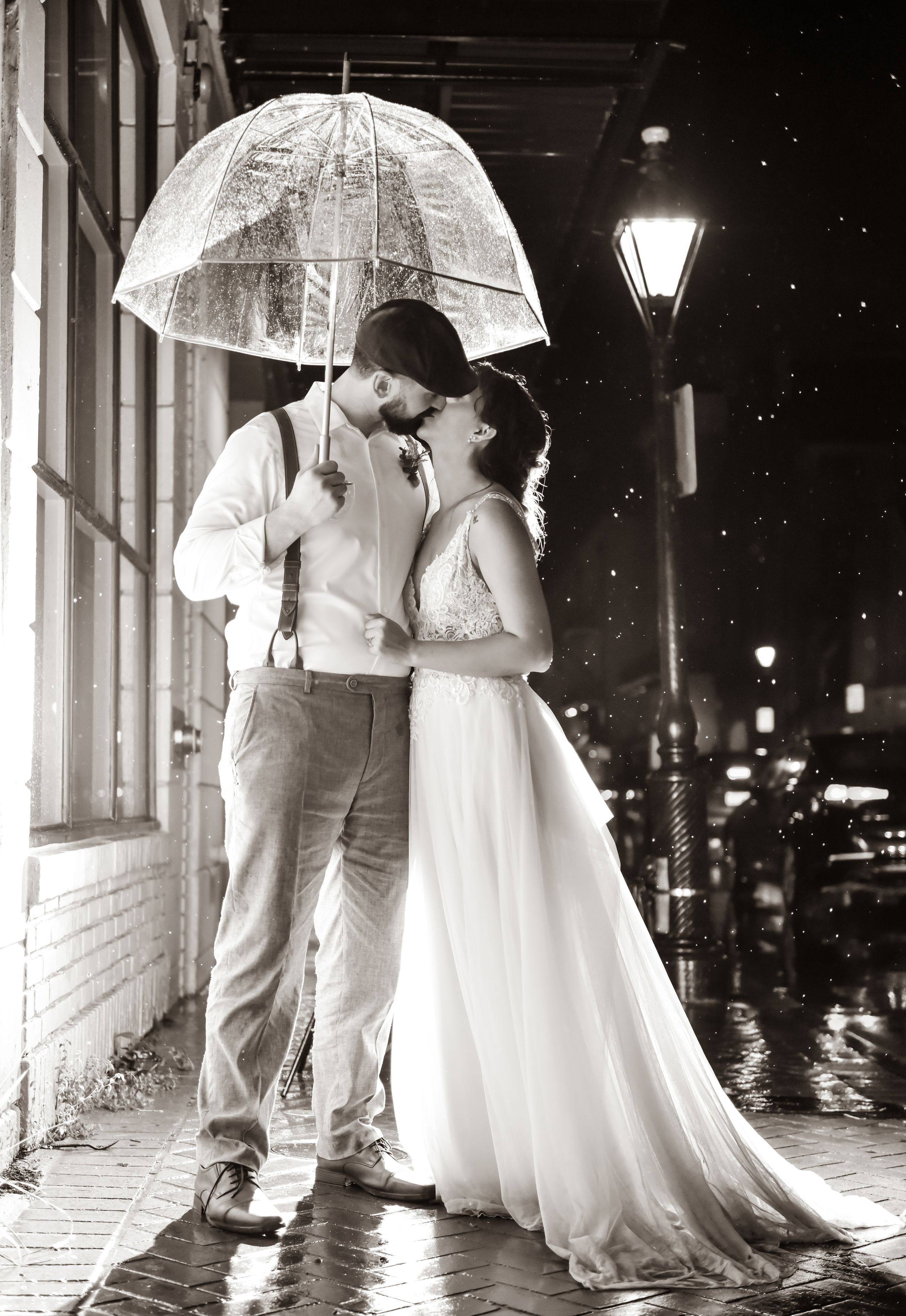 Couple sharing an intimate moment under a clear umbrella on a rainy evening with street lamps glowing.