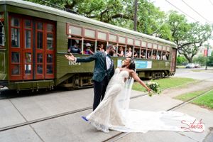 Romantic wedding photo with couple posing playfully in front of vintage green streetcar.