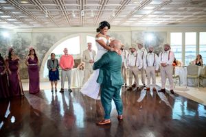 A couple performs their first dance at a wedding reception while guests watch in a bright indoor venue.