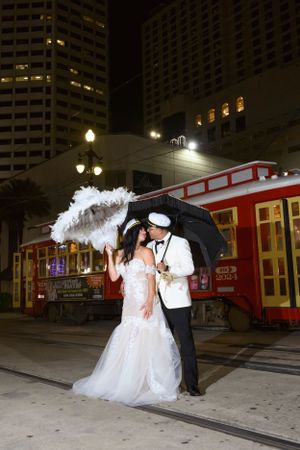 Newlyweds share romantic moment with parasol in front of vintage red streetcar at night.