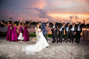 Wedding party poses for sunset photo with bridesmaids in pink and groomsmen celebrating.