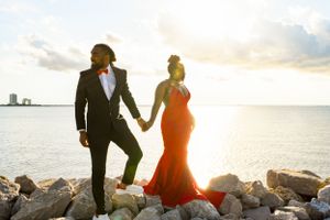 Sunset silhouette of couple on rocky shoreline with warm golden light and ocean backdrop.