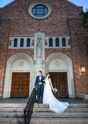 Architectural wedding portrait on the steps of a beautiful brick church with round window and ornate doors.