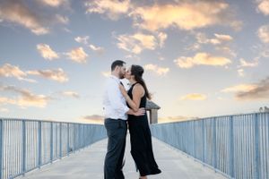 A tender sunset moment between a couple on a white bridge overlooking the water.