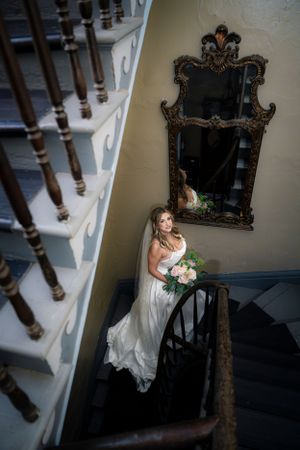 An elegant bridal portrait on vintage stairs with an ornate mirror and white banister.