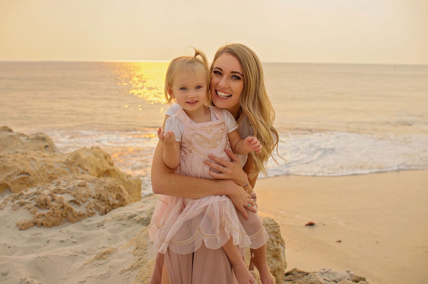 mother holding young daughter on beach smiling with sunset