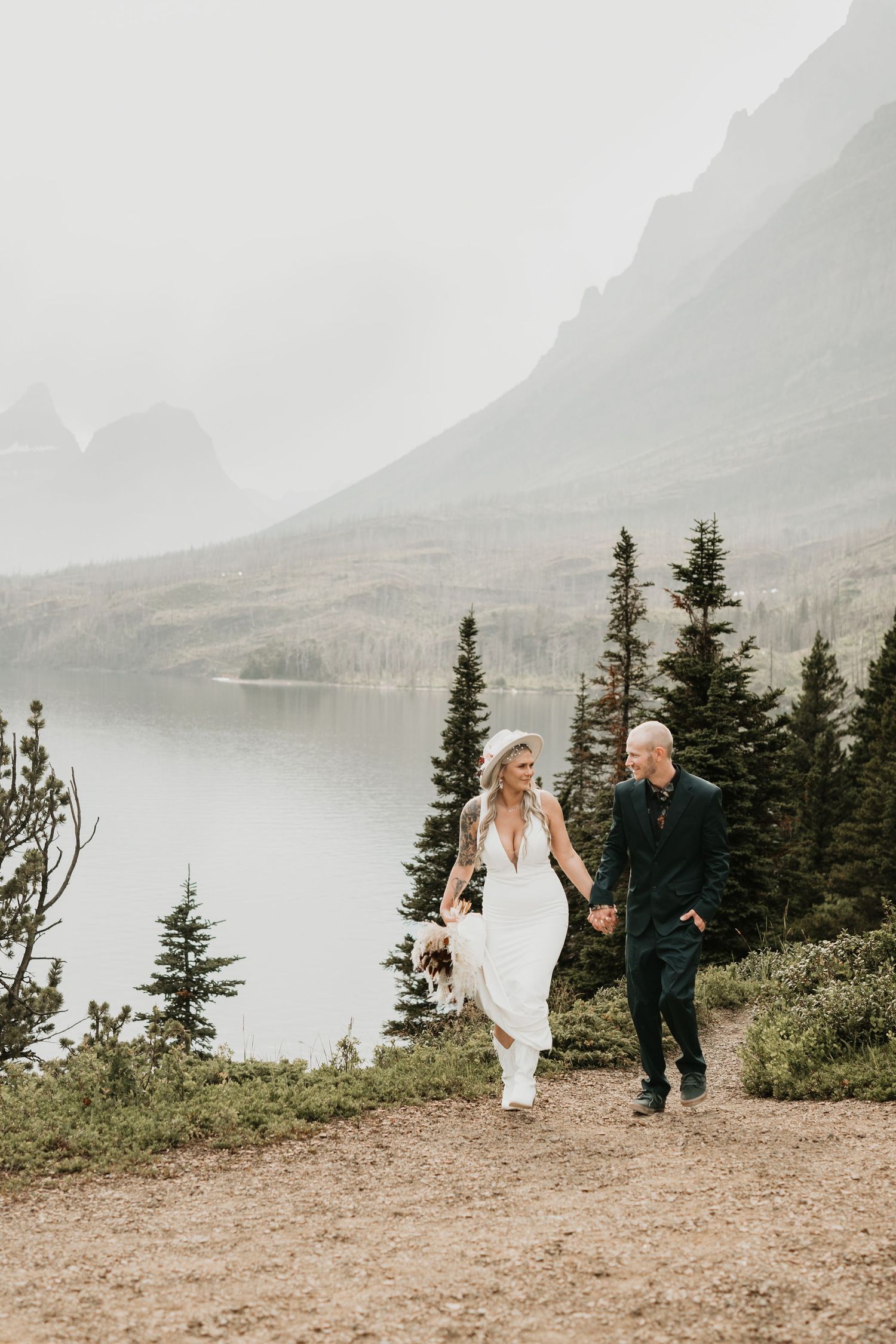 Newlyweds walking hand in hand along misty mountain trail.