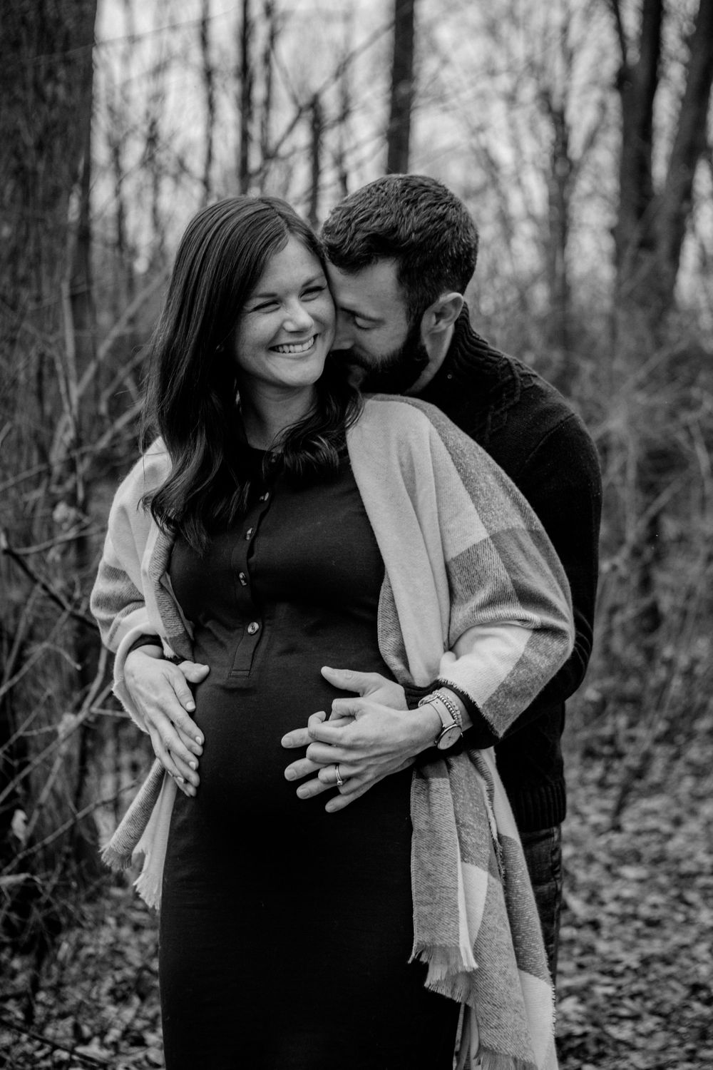 A romantic maternity photo session in a wooded forest setting showing a tender embrace in black and white.