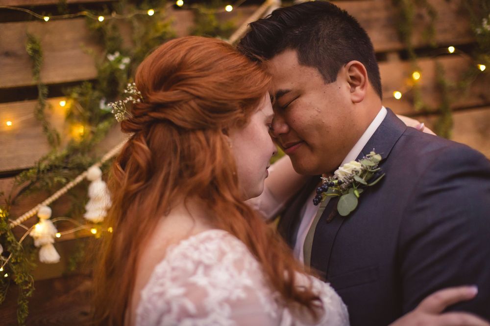 An intimate moment between newlyweds with twinkling lights and greenery in the background.