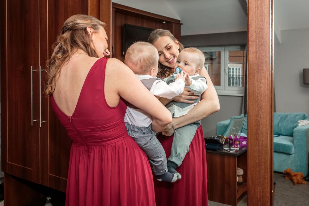 bridesmaid lifts the baby up in front of the full length mirror to see himself