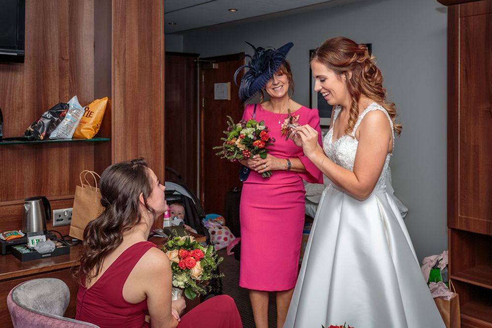 bride looking at a button hole smiling as her mum holds up her bouquet