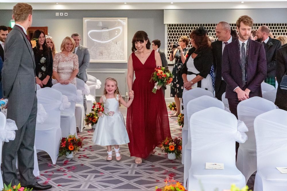 flower girl walks up the aisle holding hands with a bridesmaid