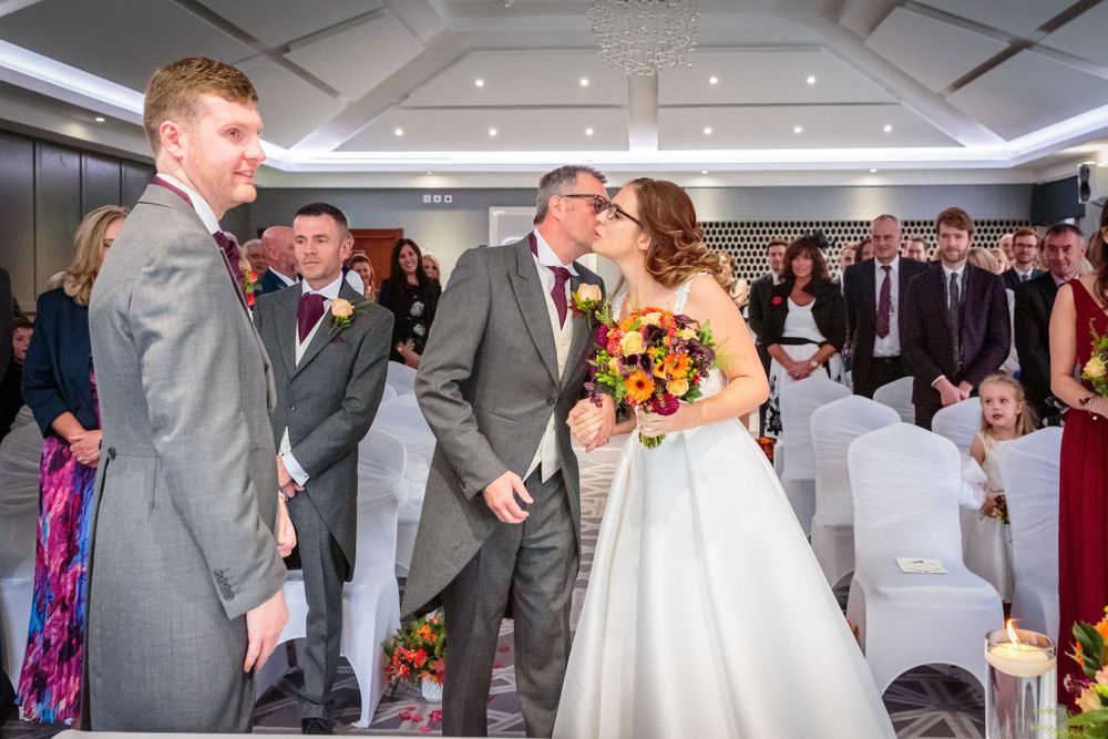 bride gets a kiss on the cheek from her father as they reach the end of the aisle