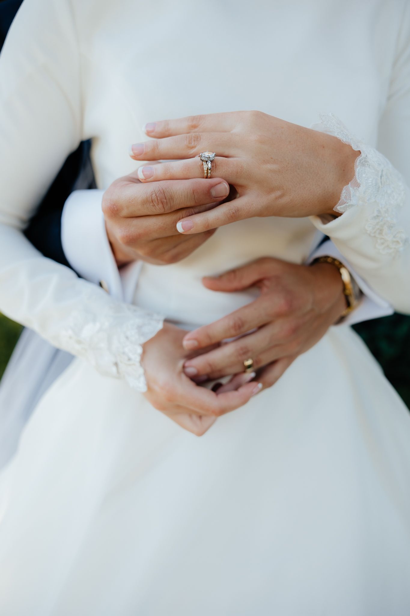 Delicate close-up of engagement ring and wedding band on bride's hand with lace sleeve details.
