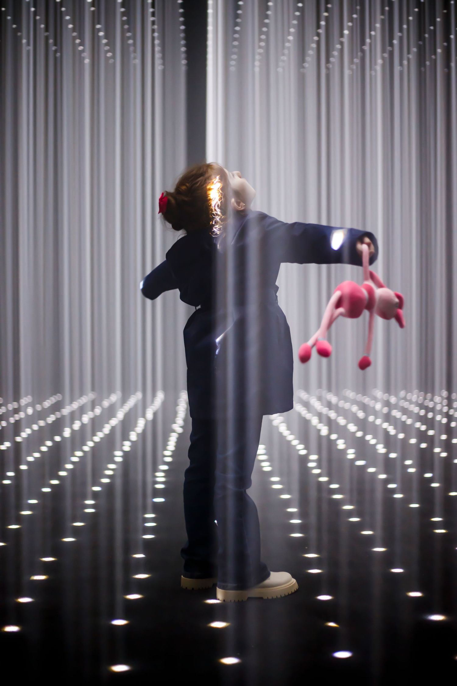 Silhouette of figure in dark clothing holding pink objects against illuminated vertical light installation.