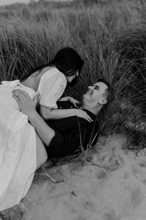 Intimate couple lying in beach grass sharing a romantic moment in black and white.