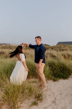 Romantic couple twirling in a dance among coastal dunes and grass.