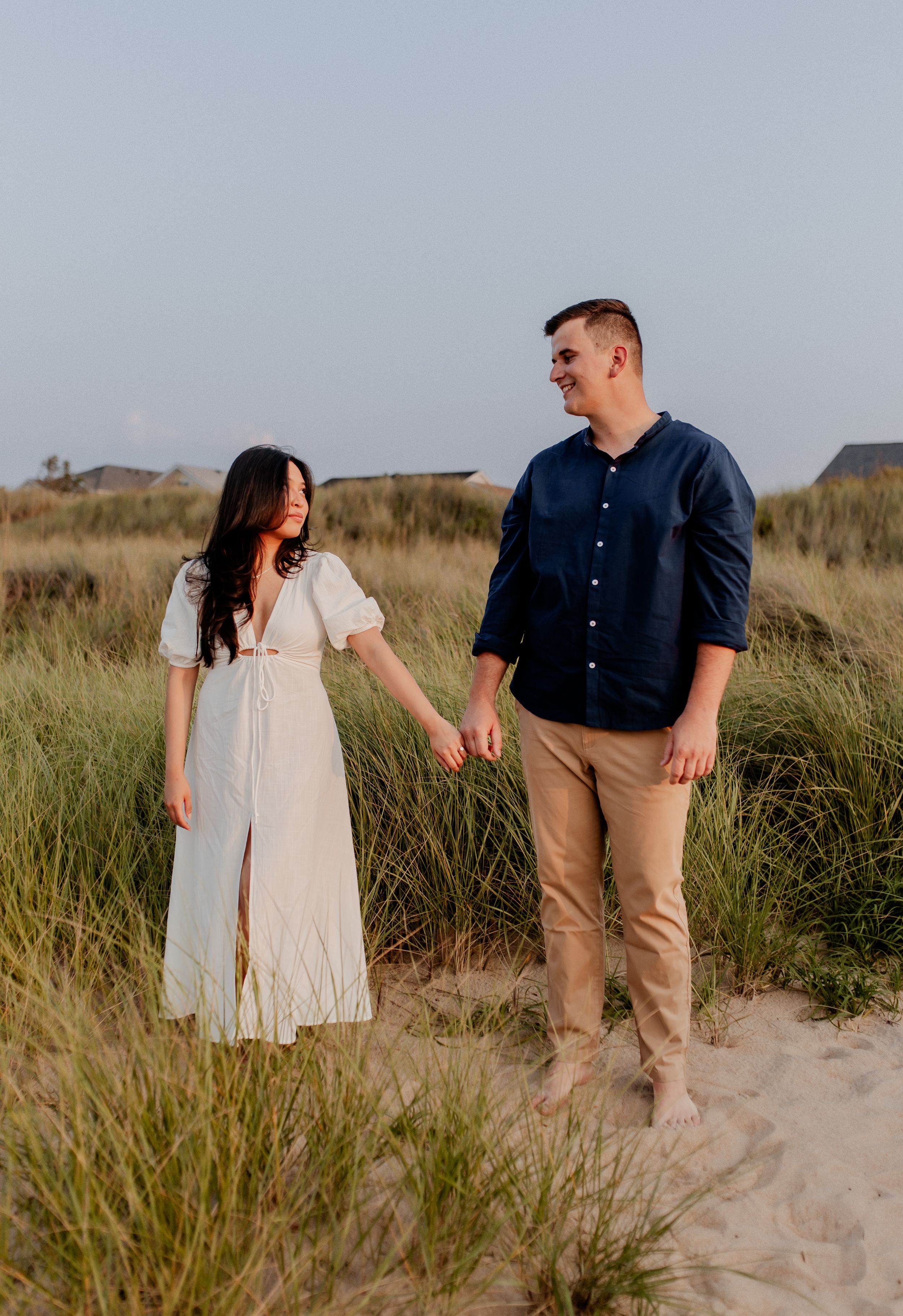 Couple in coordinated outfits standing together on sandy beach path.