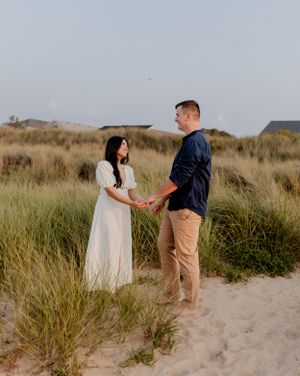 Couple holding hands in tall grass and sand dunes during golden hour.
