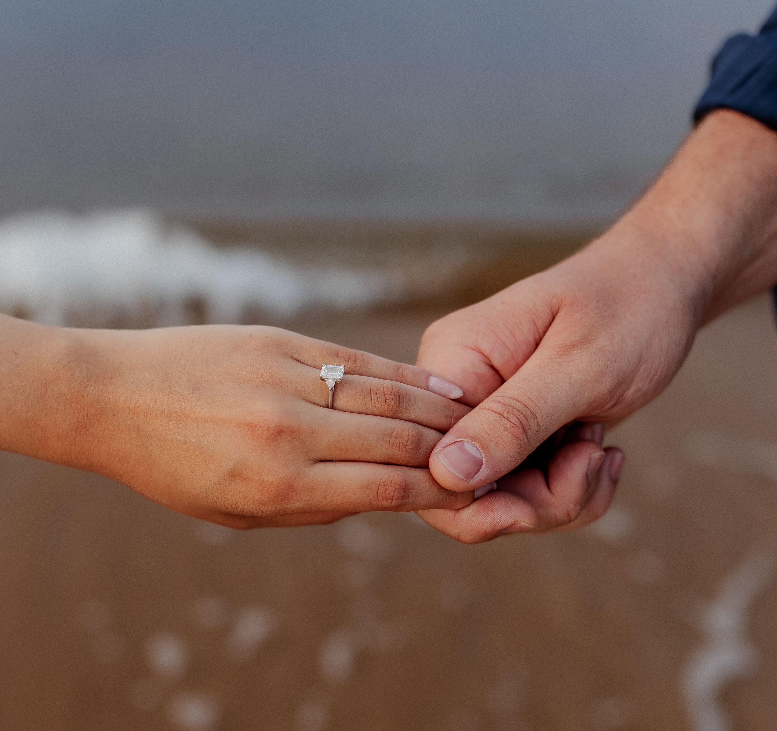 Close up of hands with engagement ring against ocean backdrop.