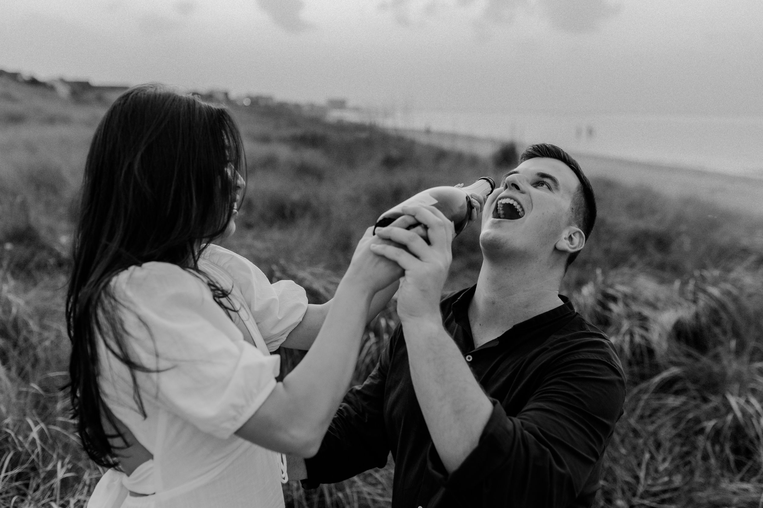Playful black and white photo of couple laughing together in beach grass.