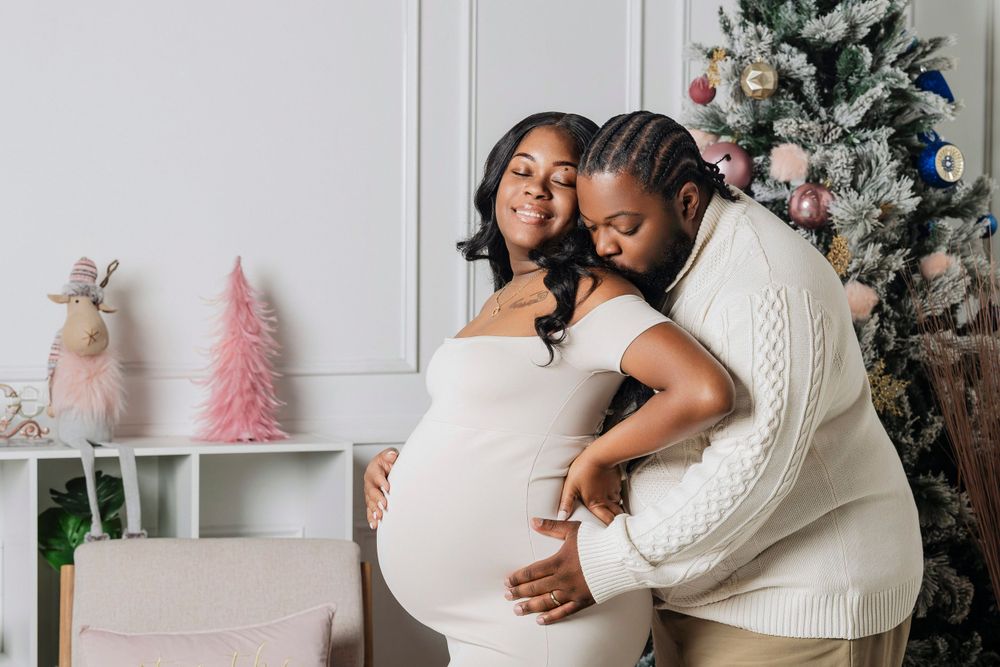 Couple sharing tender moment beside Christmas tree, man kissing pregnant woman's cheek.