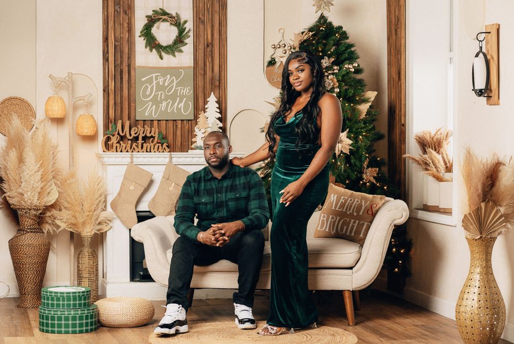 Elegant couple standing together in front of decorated Christmas tree with holiday accents.