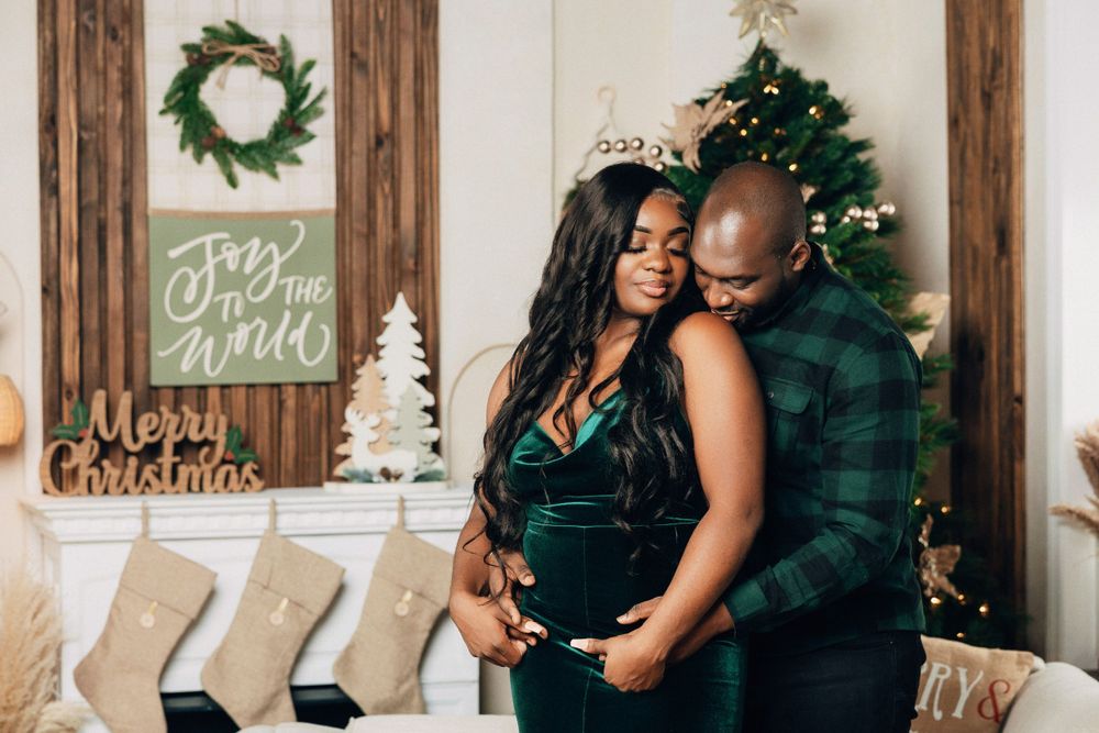 Couple sharing intimate moment beside Christmas tree with Merry Christmas sign displayed.