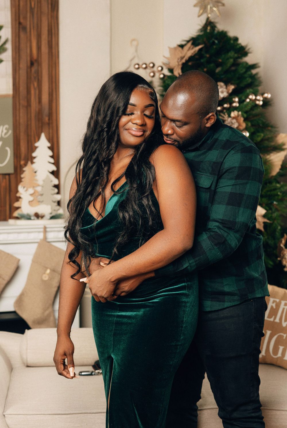 Couple in green velvet outfits embracing warmly in front of decorated Christmas tree.