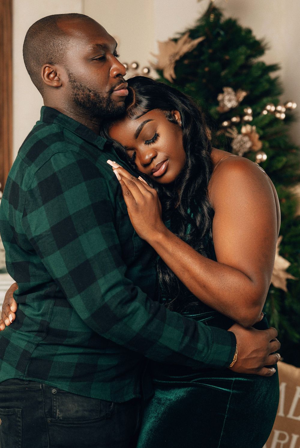 Couple in green outfits sharing close embrace in front of festive Christmas tree decor.