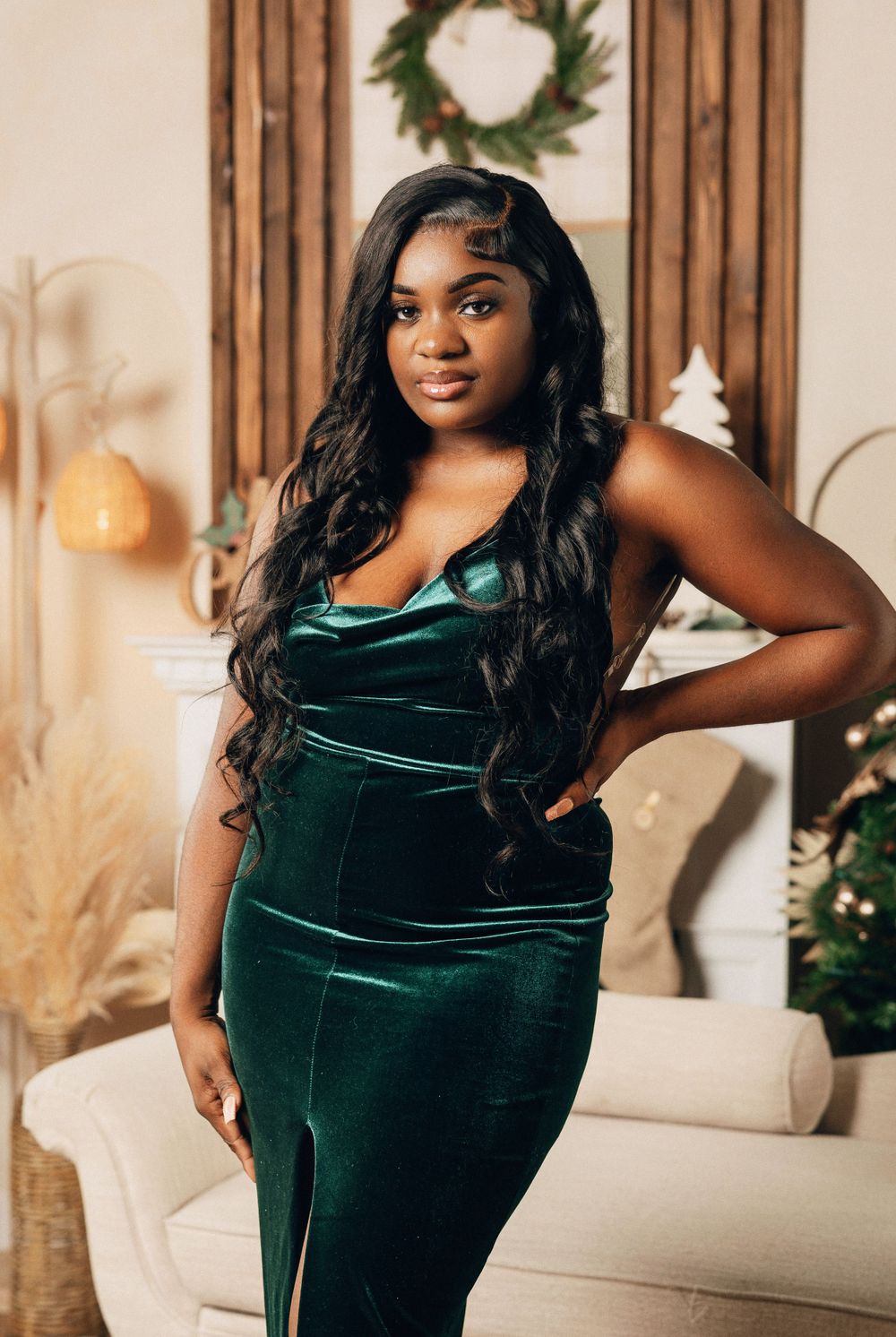 Woman in elegant emerald green velvet gown posing in festive Christmas decorated room.